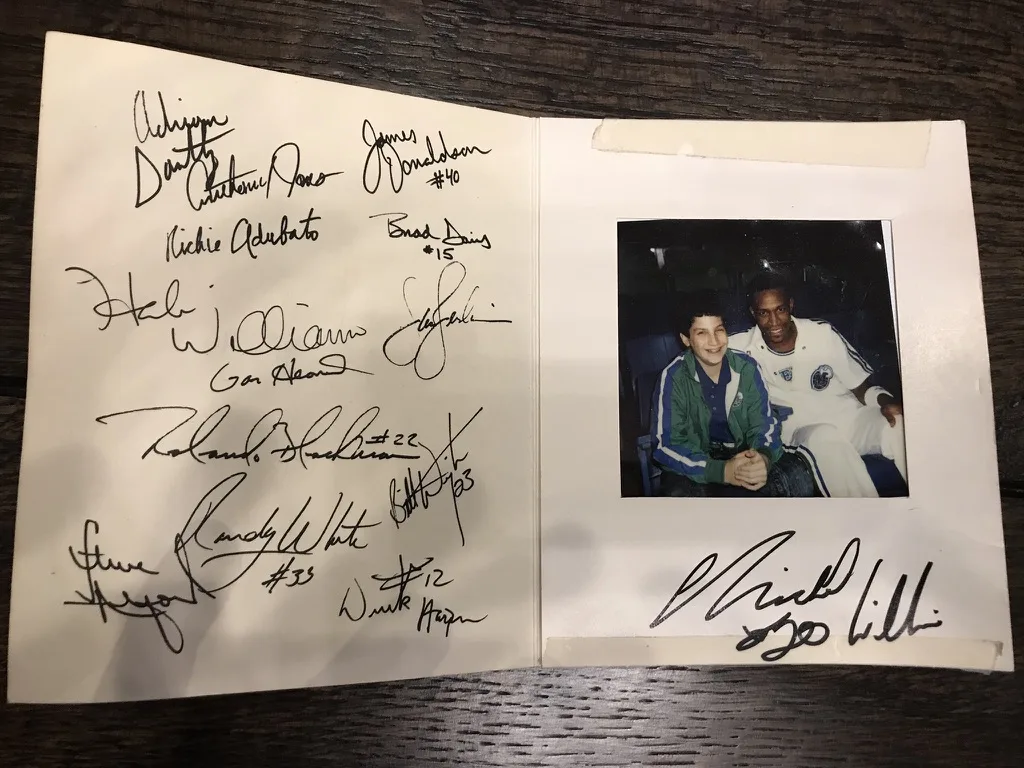 Signed Dallas Mavericks card from Andrew Jonathan Hillman's childhood as a promotions assistant and ball boy. Childhood photo of Andrew with a Mavericks player; Herb Williams autograph under the photo, plus other team signatures.