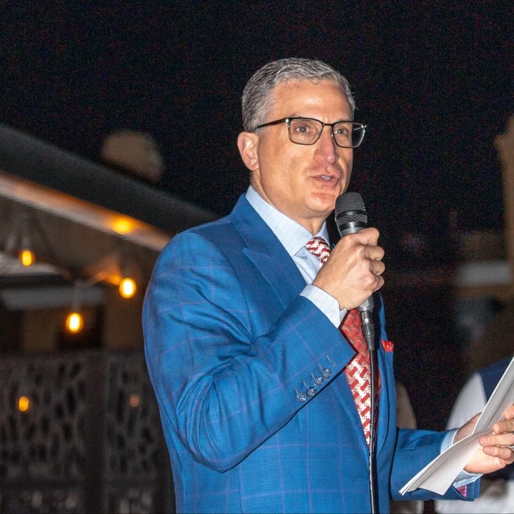 Andrew Jonathan Hillman of Dallas, Texas, speaking at an evening event in a blue plaid suit.
