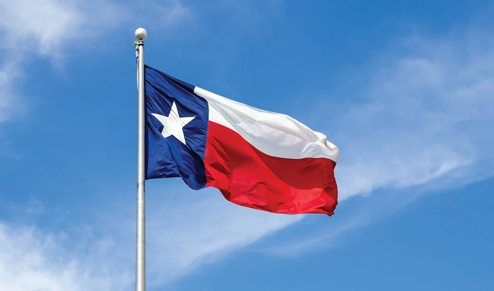 Texas flag waving under wispy clouds