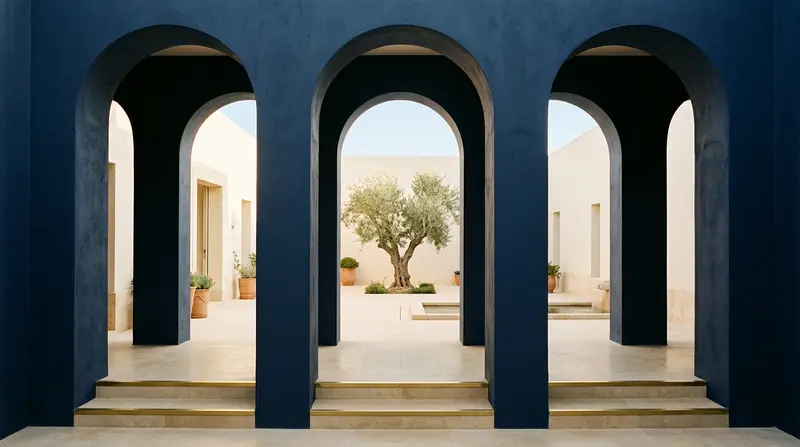 Navy arches opening onto a sunlit courtyard with an olive tree, an architectural still for Andrew Hillman's site